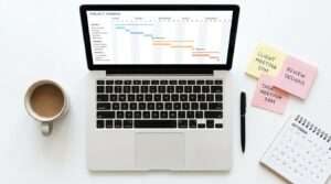 A laptop screen displaying a colorful Gantt chart with FYP milestones and timelines, surrounded by sticky notes, a calendar, and a coffee mug on a desk